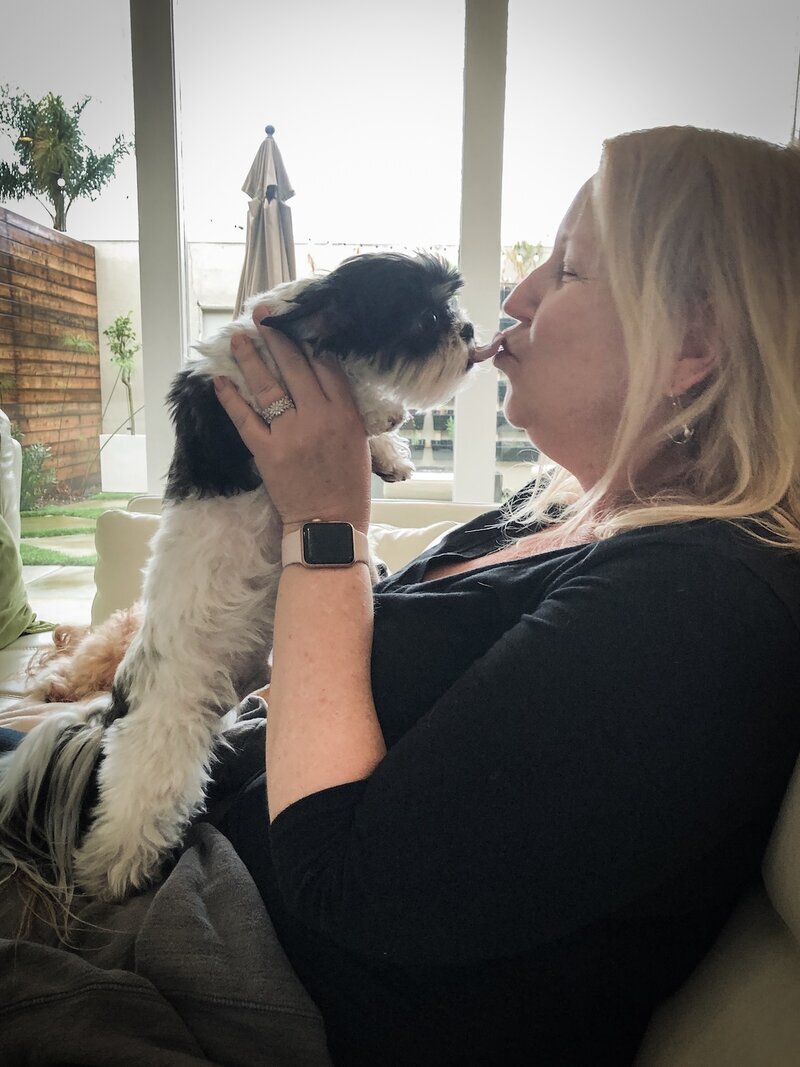 Terri cuddling a tiny black-and-white puppy in the living room at Beach House Bliss OC, Huntington Beach